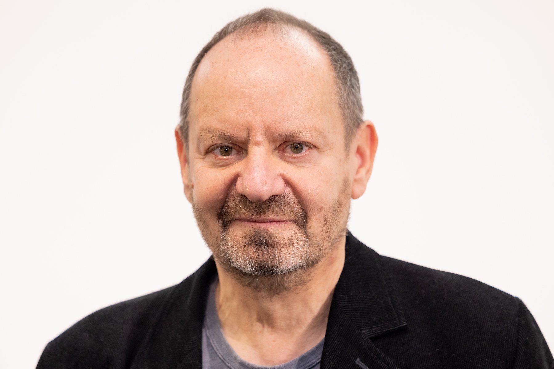 Philippe Sands, with short gray hair and a gray beard, in a black jacket against a white background