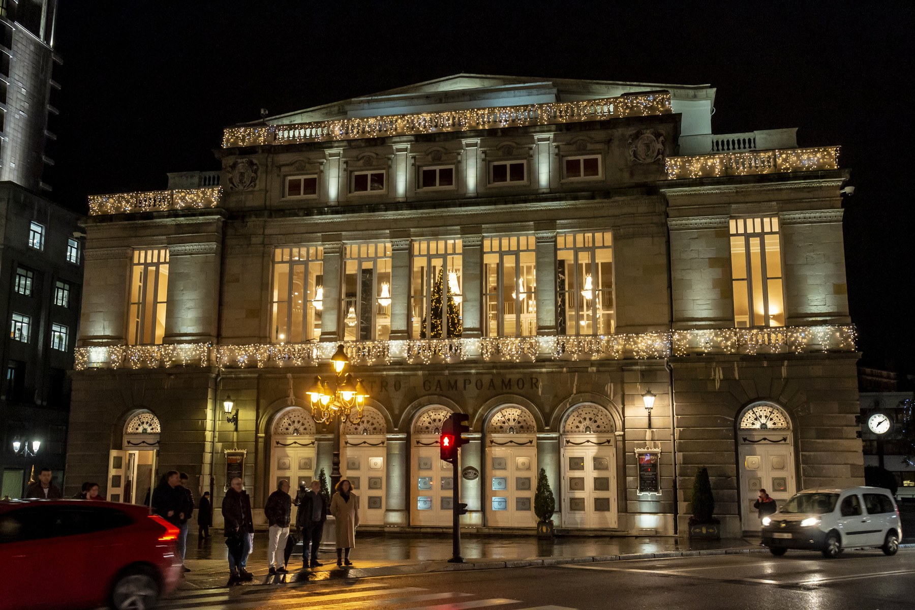The stone facade of the Campoamor Theater in Oviedo at night, its windows lit gold and festive lights along the cornice