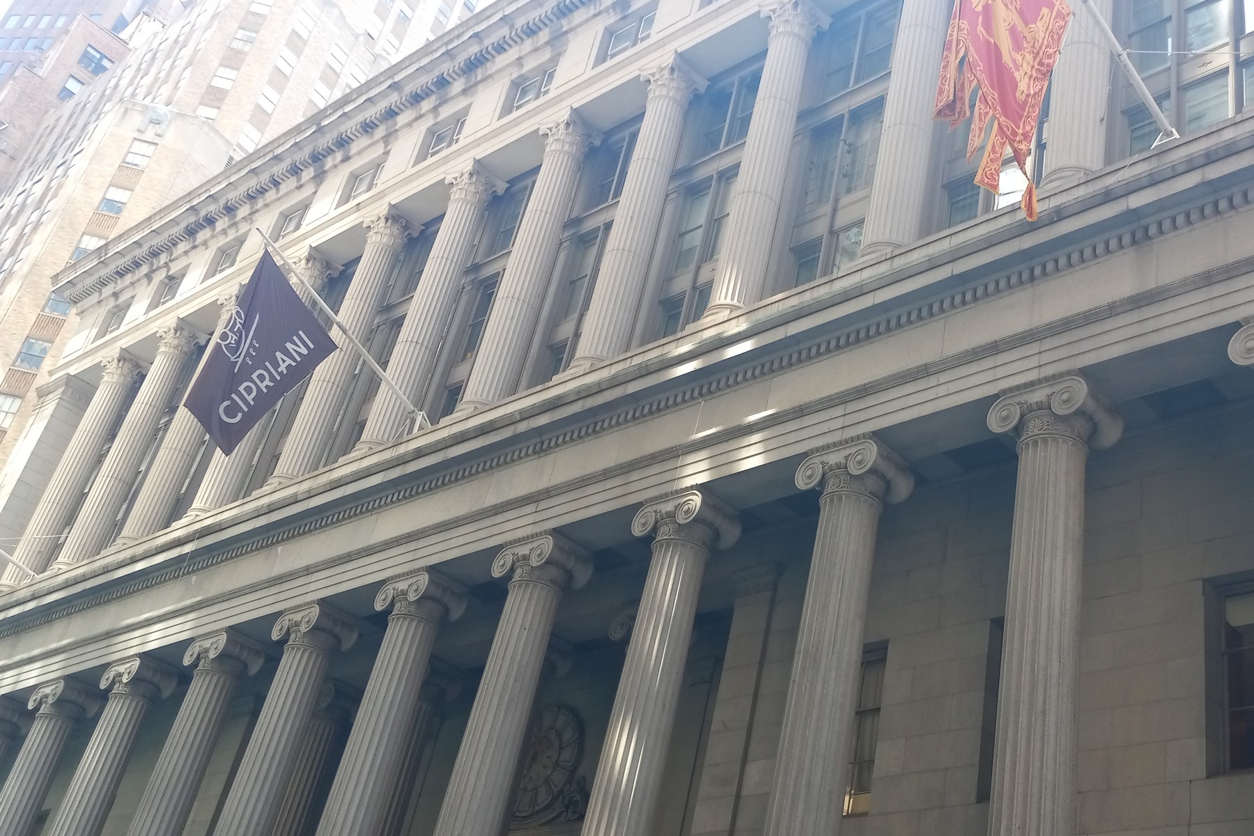 The colonnaded granite front of 55 Wall Street in Manhattan, with a Cipriani banner and a red Venetian flag